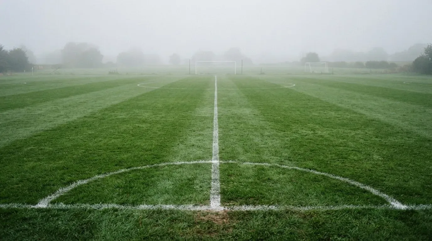 Ein leeres Fußballfeld im Morgennebel, die Mittellinie verliert sich im Dunst, kein Mensch ist zu sehen.