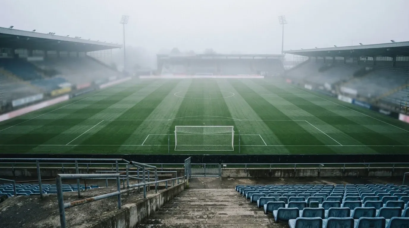 Ein Fußballfeld im Morgennebel aus erhöhter Position gesehen, Mittellinie und Tore sind sichtbar, keine Spieler auf dem Rasen.