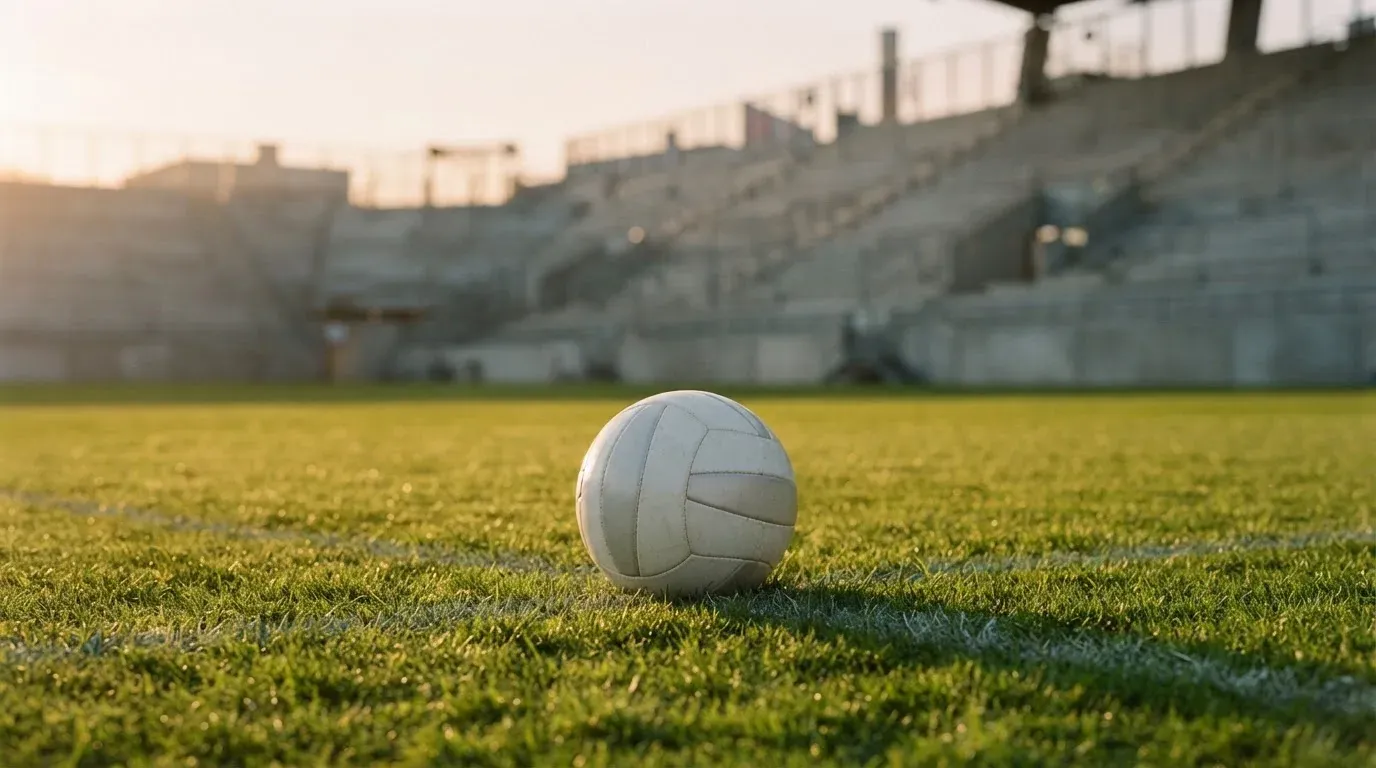 Ein Fußball liegt auf einem Rasen im Licht der tief stehenden Sonne, dahinter leere Sitzreihen.